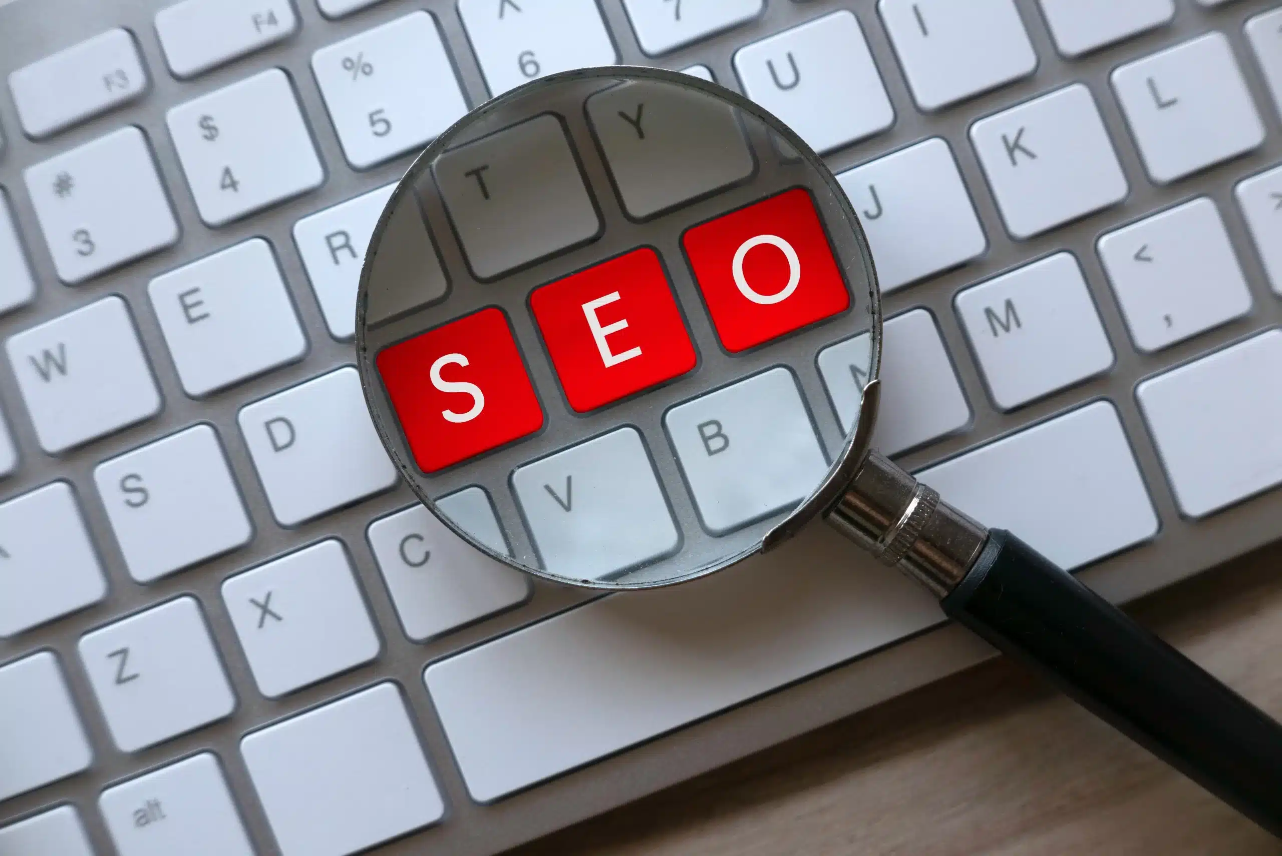 a magnifying glass sitting on top of a keyboard WITH SEO in red
