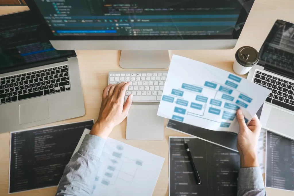 A group of people working at a desk with laptops and paper.